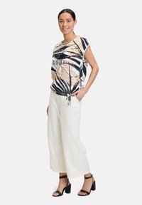 Loose-fit, short-sleeve top with a beige and black palm leaf print, accented with a drawstring at the hem. Paired with wide-leg white pants.