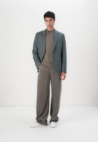 Grå blazer med subtil textur, beige crew neck-tröja och vida grå byxor, kombinerat med vita sneakers. Enkelt, modernt design.