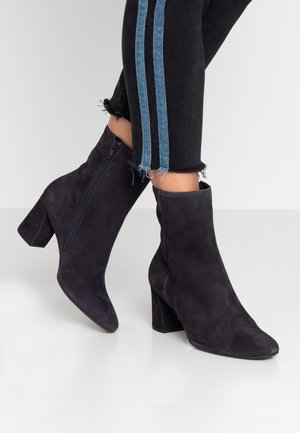 Bottes chevilles en daim noir à talons blocs portées avec un pantalon noir doté de bandes latérales bleues et d'ourlets effilochés.