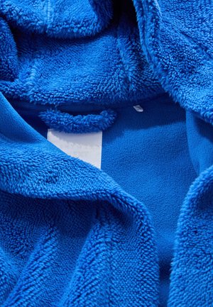 Helles blaues Fleece-Stoff mit weicher, flauschiger Textur. Das Innendesign zeigt Etiketten und eine Zugschlaufe für Bequemlichkeit.