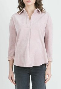 Vaaleanpunainen corduroy-paita, jossa on kauluspäällinen, pitkät hihat, jotka on käännetty hihansuista, ja hieman rento istuvuus. Paidassa on pystysuora ribbitettu rakenne.