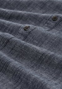 Teren de denim închis cu o textură subtilă, având două butoane negre pe marginea superioară, aranjate în straturi pliate.