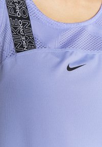 Světlofialové sportovní tílko s průsvitnou texturou, černým logem a nastavitelným popruhem s nápisem "Nike Pro".