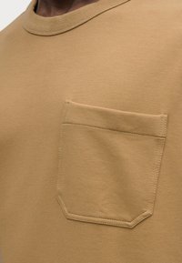 Μπεζ βαμβακερό t-shirt με στρογγυλή λαιμόκοψη και ορθογώνιο τσέπη στο στήθος με ραμμένες λεπτομέρειες. Ομαλή υφή και casual σχεδιασμός.