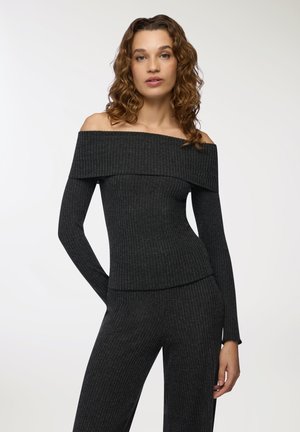 Top a spalle scoperte, in grigio scuro a coste, con maniche lunghe, caratterizzato da un ampio scollo e una silhouette aderente. Texture morbida, dettagli minimi.