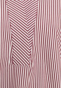 Tissu rayé bordeaux et blanc présentant un motif en chevron, avec une poche carrée intégrée dans le design. Texture lisse, matériau doux.