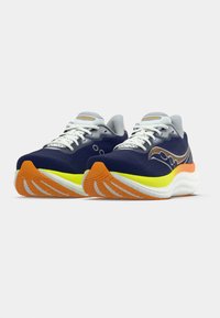 Pár tmavomodrých a šedých bežeckých topánok s bielymi šnúrkami, neonovo žltými strednými podrážkami a oranžovými štruktúrovanými vonkajšími podrážkami na bielom pozadí.