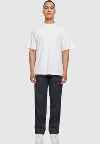 Camiseta blanca de manga corta con cuello redondo, combinada con pantalones de mezclilla oscuros y zapatillas blancas, contra un fondo neutro.