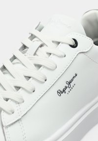 Sneaker din piele sintetică albă cu talpă din cauciuc. Prezintă șireturi albe, un ochi de șiret negru și un logo "Pepe Jeans London" pe lateral.