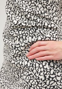 Main reposant sur la hanche, au-dessus d'un tissu à motif abstrait noir et blanc d'un vêtement ajusté.