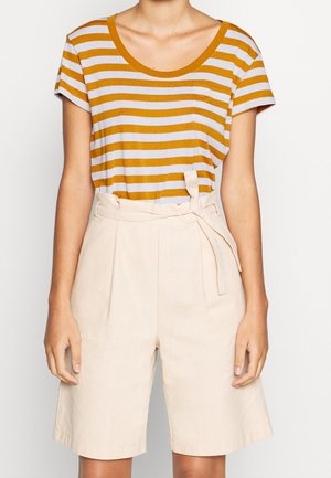 Camiseta de rayas en colores mostaza y lavanda, combinada con pantalones cortos beige de talle alto con cinturón de lazo y detalle de pliegues en el frente.