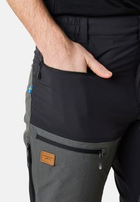 Pantalons multi-poches noirs et gris avec fermeture éclair, tissu texturé et une étiquette beige avec un logo. Accent du drapeau suédois sur le côté.