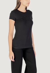 Camiseta negra de manga corta con escote redondo, con letras de strass en el frontal. Combinada con pantalones negros. Textura de tela suave.