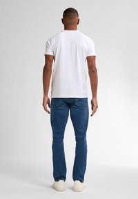 Camiseta blanca de algodón de manga corta, combinada con jeans de mezclilla azul. Los jeans presentan un corte estándar y dos bolsillos traseros.