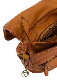 Tan leren handtas met ritssluitingen, zichtbare stiksels en een metalen sieraad. Zacht, gestructureerd oppervlak met een slungelige vorm.