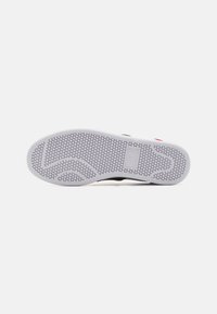 Gummisåle til sneakers med et teksturert honningkake-mønster, hovedsakelig hvit med svarte detaljer. Har en logo og flerfargede elementer.