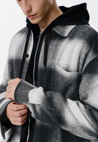 Jakna crno-bijelog karo uzorka s mekanom teksturom, s prednjim dijelom na kopčanje, patentnim zatvaračem i unutarnjim slojem s kapuljačom u crnoj boji.