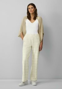 Leichter beiger Cardigan über einem weißen, figurnahen Top, kombiniert mit weichen, strukturierten cremefarbenen Hosen mit einem subtilen Karomuster und elastischem Bund.