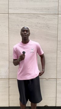 Camiseta de algodón rosa con un gráfico de un personaje de dibujos animados en el pecho izquierdo, combinada con pantalones cortos negros hasta la rodilla. El sujeto sostiene un micrófono.