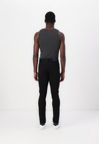 Black slim-fit jeans with a smooth texture and five-pocket design, paired with a dark gray ribbed tank top. White shoes visible at the bottom.