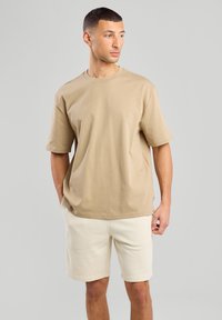T-shirt in cotone beige con maniche corte e scollatura rotonda, abbinata a pantaloni corti beige chiaro, caratterizzati da una vestibilità comoda e un design minimalista.
