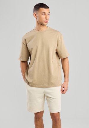 Beige Baumwoll-T-Shirt mit kurzen Ärmeln und rundem Halsausschnitt, kombiniert mit hellbeigen Shorts, die eine lockere Passform und ein minimalistisches Design aufweisen.