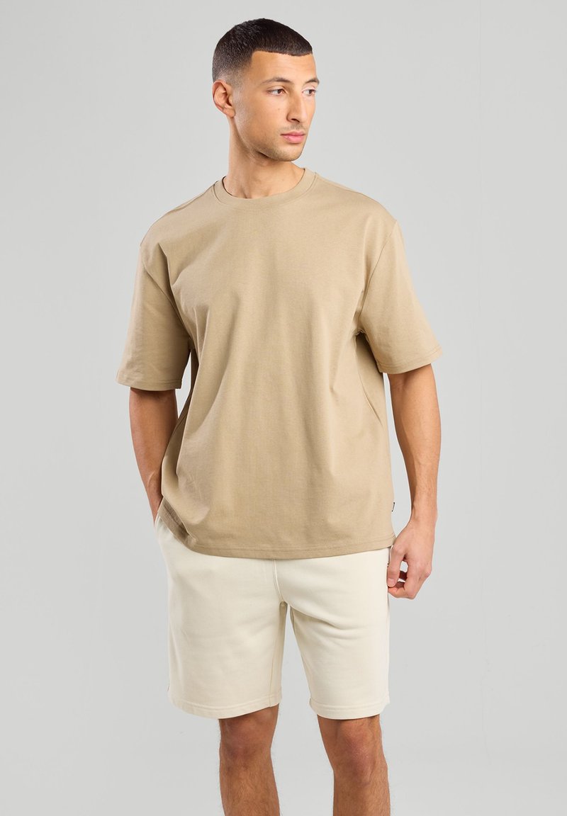 T-shirt in cotone beige con maniche corte e scollatura rotonda, abbinata a pantaloni corti beige chiaro, caratterizzati da una vestibilità comoda e un design minimalista.