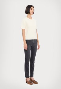 Weißes Rippstrick-Top mit kurzen Ärmeln, kombiniert mit dunkelgrauen, enganliegenden Hosen und braunen, bequemen Loafers mit Absatz und strukturiertem Akzent.