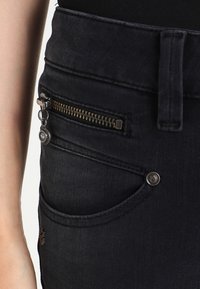 Svarta denimjeans med en dragkedjeficka, metallaccenter och en slät yta. Designade med en figurn ära silhuett och hållbara sömmar.