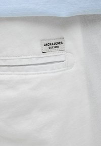 Fehér textúrált anyag, melynek díszített zsebe van, és jól látható címkéje olvasható: "JACK & JONES EST.1990."