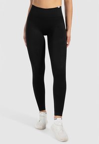 Sorte leggings lavet af strækstof med høj talje og glat tekstur, kombineret med hvide sportssko.