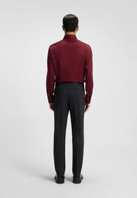 Camicia a maniche lunghe color bordeaux con colletto classico, abbinata a pantaloni scuri su misura. Tessuto morbido con una vestibilità elegante e polsini bottonati.