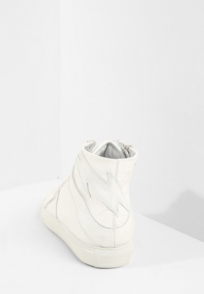 Baskets montantes en cuir blanc avec un design de coutures surélevées, texture lisse et fermeture éclair à l'arrière. Semelle en caoutchouc.