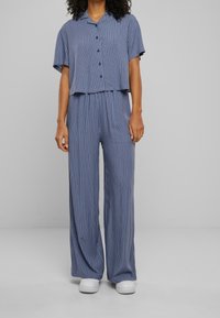 Ensemble deux pièces rayé dans des tons bleus, composé d'une chemise courte à boutons et d'un pantalon à jambes larges, fabriqué en tissu léger.