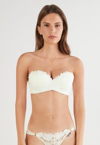 Vit bandeau-bh med blommig spetsdetalj, slät tygkvalitet och en välarbetad passform. Matchande trosor i spets med blommönster.