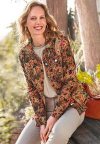 Denim jacket met bloemenpatroon in warme kleuren, metalen knopen en een getailleerd ontwerp. Gecombineerd met een lichte top en beige broek.