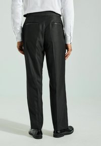 Pantalones negros ajustados con una textura suave, con dobles bolsillos traseros y un corte slim. Combinados con zapatos de vestir negros brillantes.