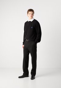 Pulover negru din tricot cu model cu caneluri, purtat peste o cămașă albă cu guler, asortat cu pantaloni negri și pantofi negri, având un accent albastru pe pulover.