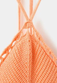 Gros plan d'un tissu tricoté couleur pêche avec de fines bretelles et un détail en crochet ouvert au centre en haut.