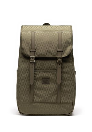 Sac à dos kaki en tissu à motif losange, rabat avant, deux sangles à boucle, poches latérales et petite étiquette logo sur le devant, sur fond blanc.