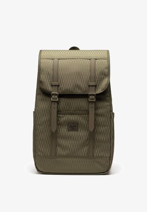 Sac à dos kaki en tissu à motif losange, rabat avant, deux sangles à boucle, poches latérales et petite étiquette logo sur le devant, sur fond blanc.