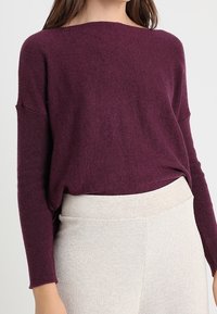 Pull en tricot bordeaux avec une coupe décontractée, un col bateau et des manches longues, associé à un pantalon texturé beige taille haute.