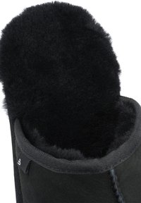 Black boot featuring a textured suede exterior, soft black fur lining, and a stitched edge. The interior maintains a thick, plush appearance.