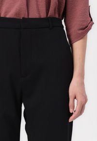 Zwarte op maat gemaakte broeken met een gladde textuur, met een vlakke voorkant en zijzakken. Gecombineerd met een losvallende, mauve top.