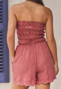 Brauner trägerloser Jumpsuit mit strukturiertem gesmoktem Oberteil und gewelltem Saum. Verfügt über seitliche Taschen und einen weichen, leichten Stoff.