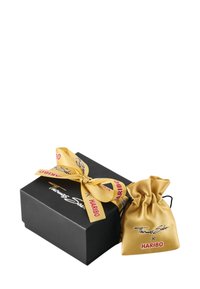 Zwarte geschenkdoos met een gouden satijnen tas die is vastgebonden met een bijpassende strik. De tas heeft logo's van "Thomas Sabo" en "HARIBO."