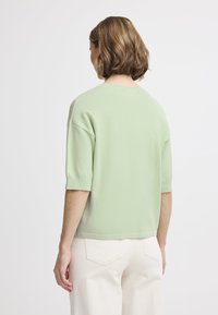 Maglione a maniche corte, verde menta, realizzato in un morbido materiale a maglia con una vestibilità rilassata e orlo arrotondato, abbinato a pantaloni a gamba larga color avorio.
