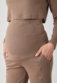 Priliehavý hnedý rebrovaný dvojdielny outfit, ktorý obsahuje skrátený top a nohavice vysokého pásu so bočnými vreckami, zdôrazňujúci jemnú textúru.