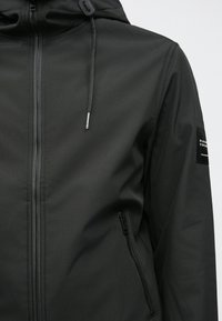 Juodas nepralaidus vandeniui džemperis su aukštu apykakle, reguliuojama kapišonu ir užtraukiamais kišenėmis. Tekstūruotas audinys su sklandžiu paviršiumi ir elegantiškas dizainas.