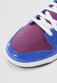 Lila och blå patentläder sneakers med vita snören, rund tå, perforerad tåkapsel och kontrasterande sömmar längs kanterna.